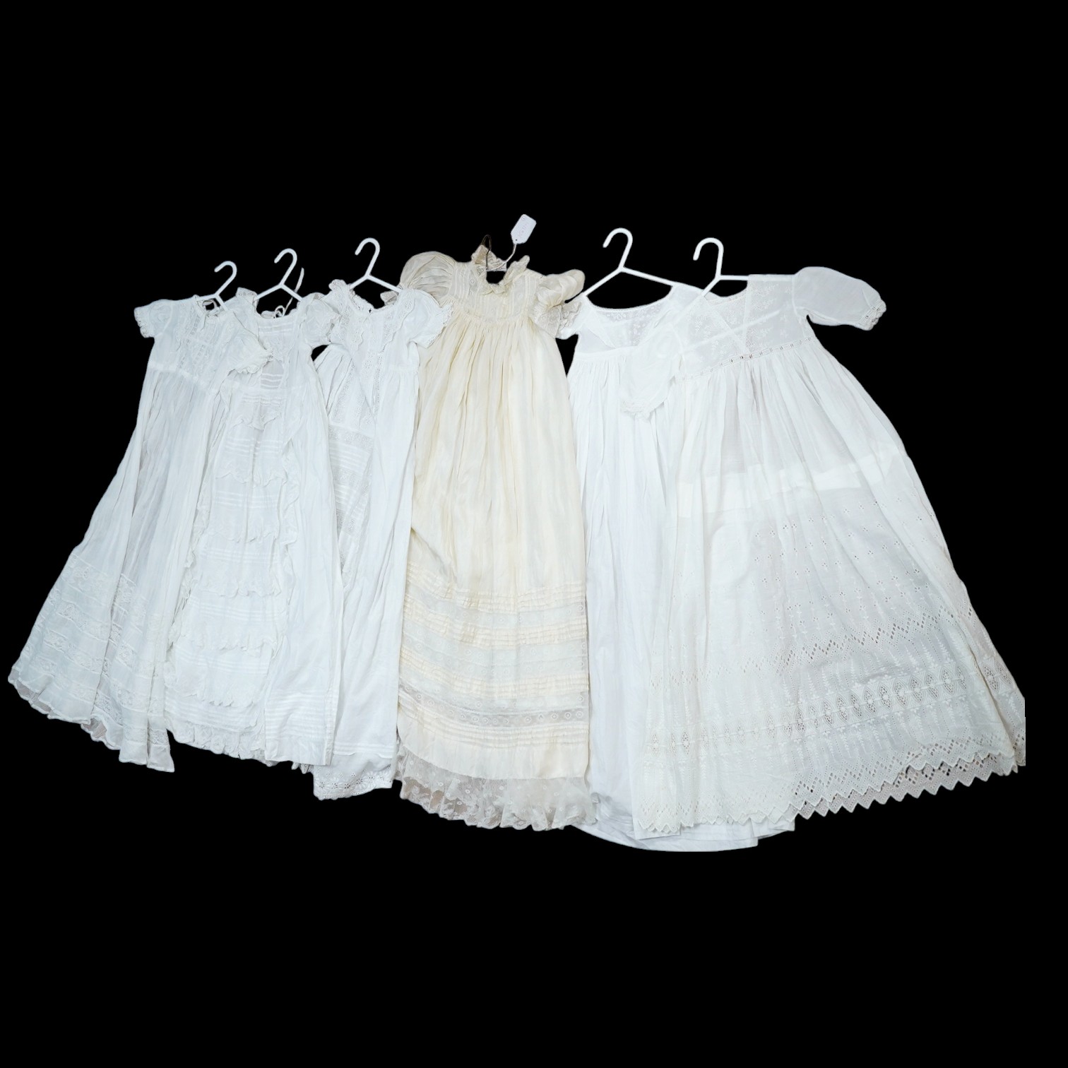 An Edwardian cream silk christening gown, together with four white christening gowns and a baby gown. The silk christening gown edged and inserted with lace and feather stitch embroidery, one Christening gown worked with